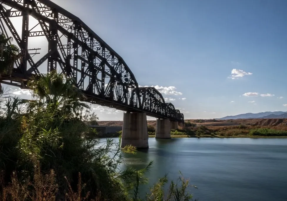 A bridge over water with trees in the foreground.